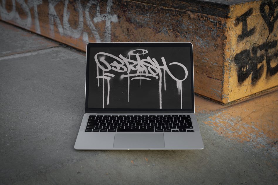 MacBook against rusty metal showing graffiti style design on dark screen